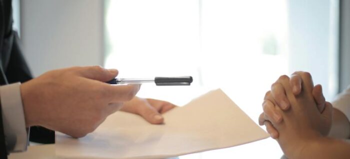 man handing a renewed policy and a pen to a woman