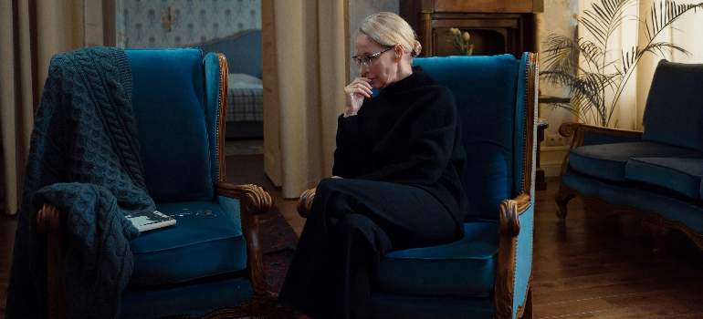 an elderly woman sitting on a couch thinking about social tips for seniors after relocating
