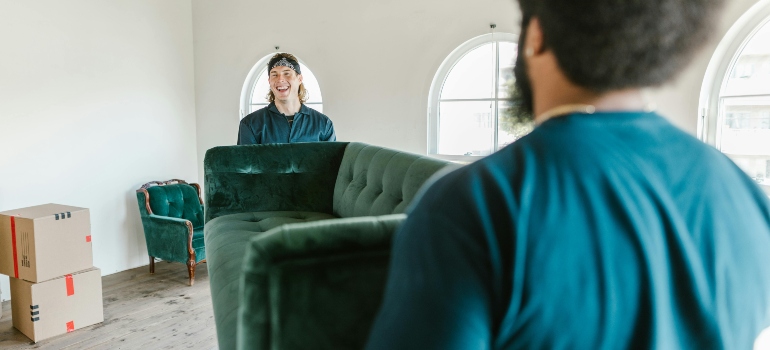 Two men in a blue t-shirt are carrying a couch 