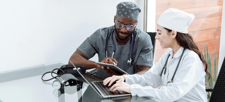 A man and a woman doctor are sitting at the table and looking at their laptop.