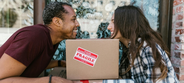 The man and the woman are looking at each other while holding their chins on the box, thinking about their movers in Reston.