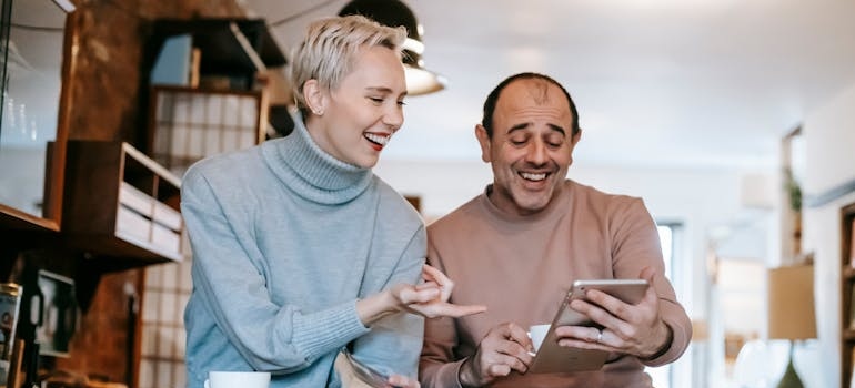 Joyful spouses laughing while watching funny movie on tablet