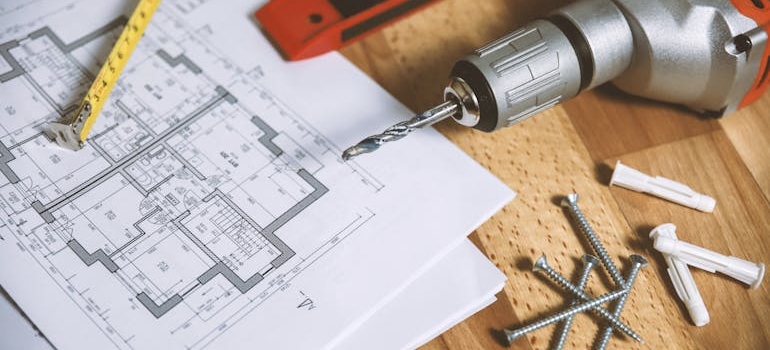 Floor plan and a drill on a wooden table.