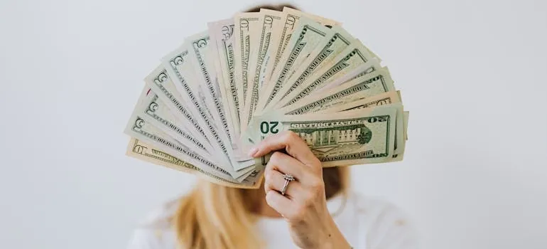 Woman Holding Fan of US Dollar Bills Wondering about The Hidden Costs of Choosing the Cheapest Rates